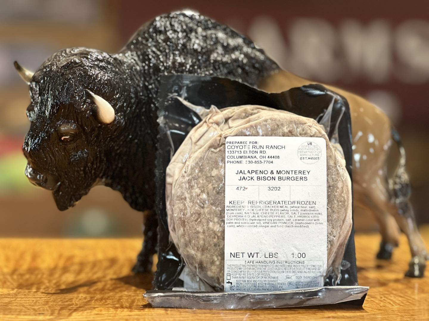 Jalapeño and Monterey Jack bison burgers packaged with a label displaying ingredients and storage instructions, alongside a decorative bison figurine on a wooden surface.