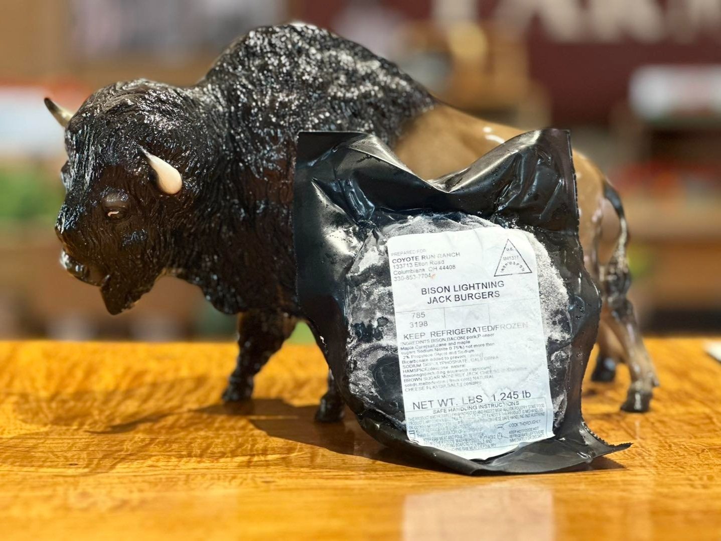 Bison Lightning Jack Burgers package displayed next to a bison figurine on a wooden table, showcasing unique bison meat product from Coyote Run Ranch, emphasizing quality and freshness.
