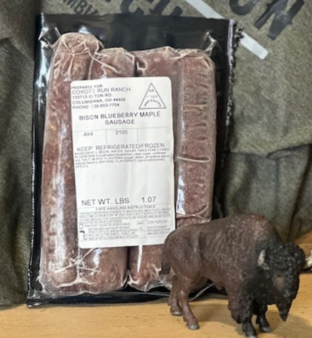 Bison blueberry maple sausage package from Coyote Run Ranch, featuring a small bison figurine and a textured background. The sausage is labeled with weight and storage instructions.