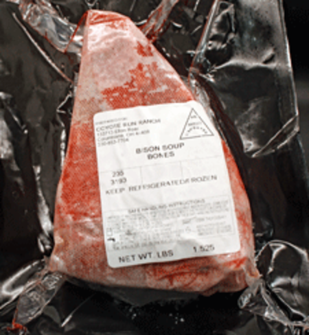 Bison soup bones packaged in a vacuum-sealed bag with a label indicating weight and storage instructions, set against a dark background.